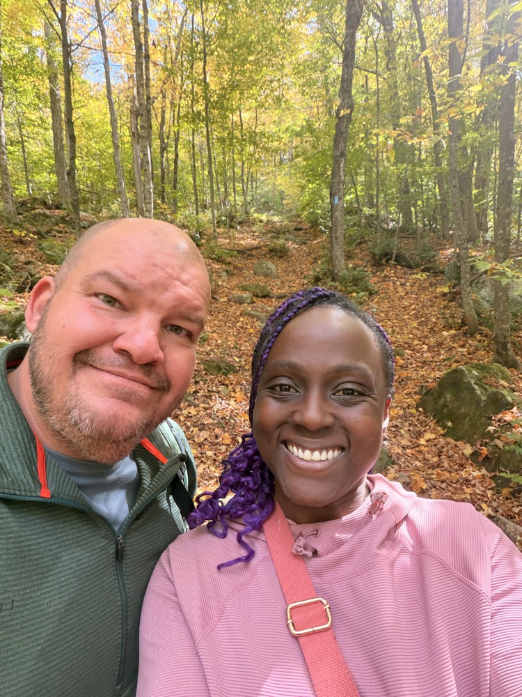 Jerneice and Aaron smiling together on a wooded trail in autumn
