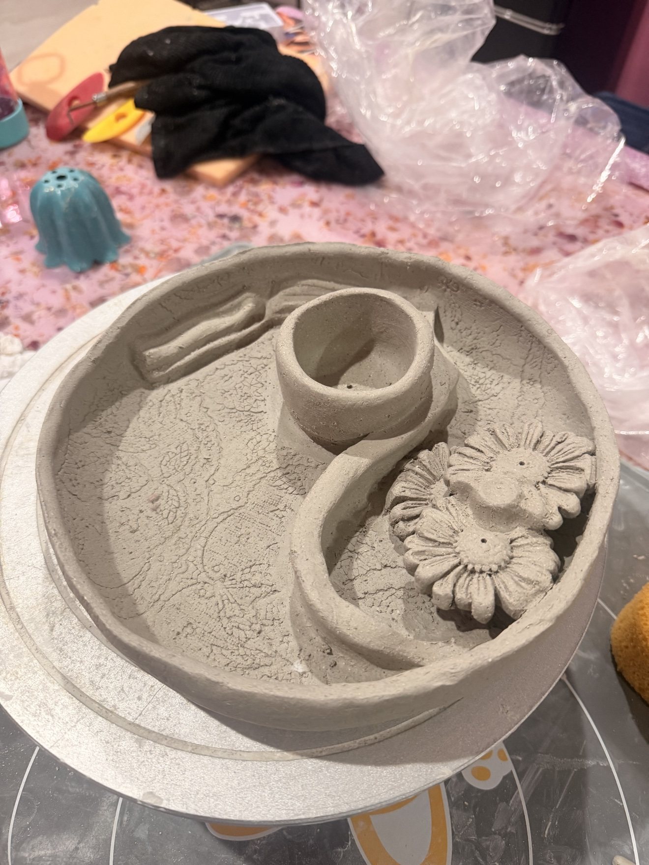An unfired clay tray with sculpted flowers and tools on the worktable